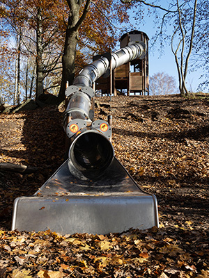 Großes UniPlay-Spielplatzgerät mit einer großen Röhrenrutsche, das mit der Umgebung des Parks und den natürlichen Hängen zusammenarbeitet, um ein maßgeschneidertes Gerät zu bauen.